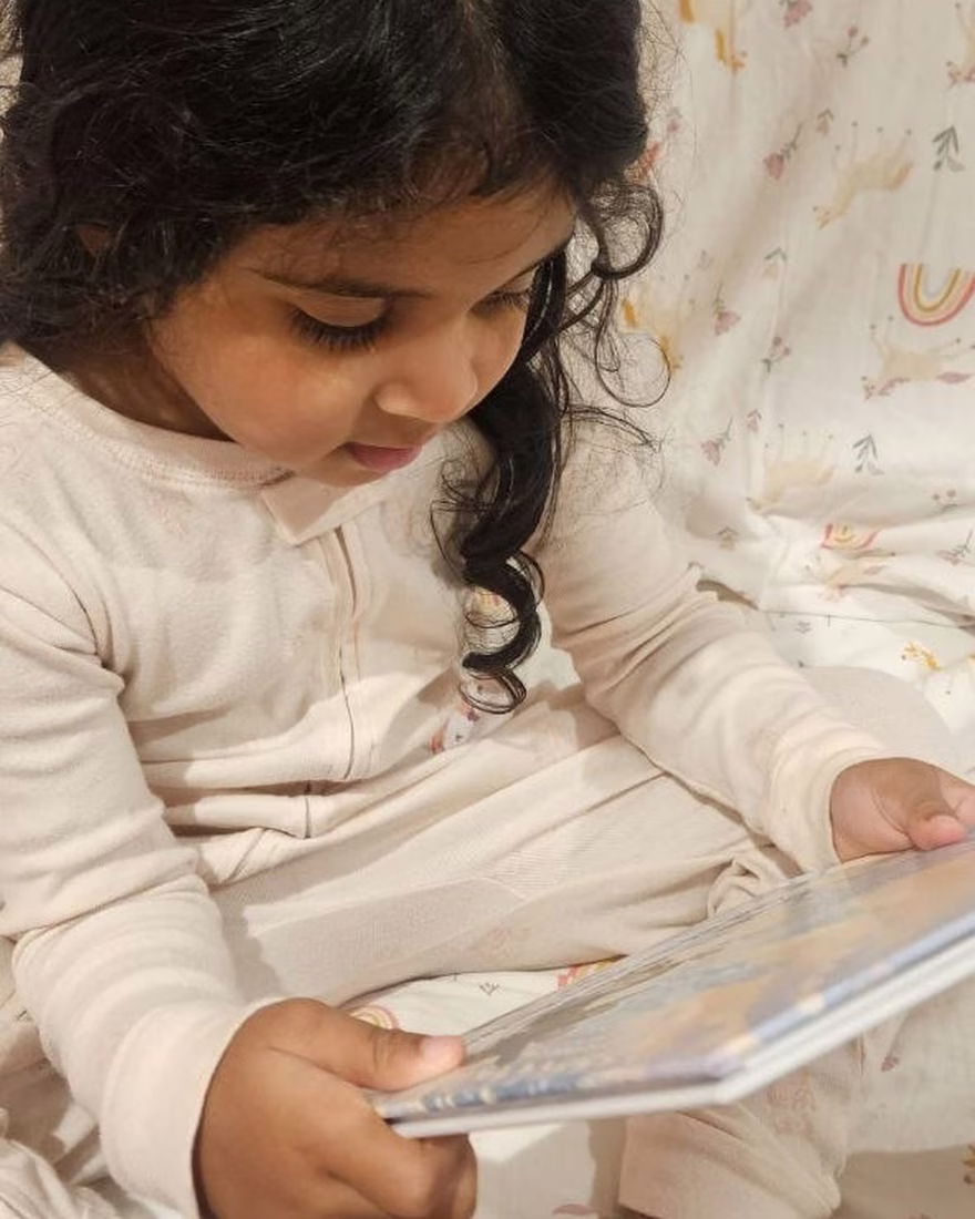 Chloe sitting up in bed, turning the pages of her personalized Story Genie hardcover