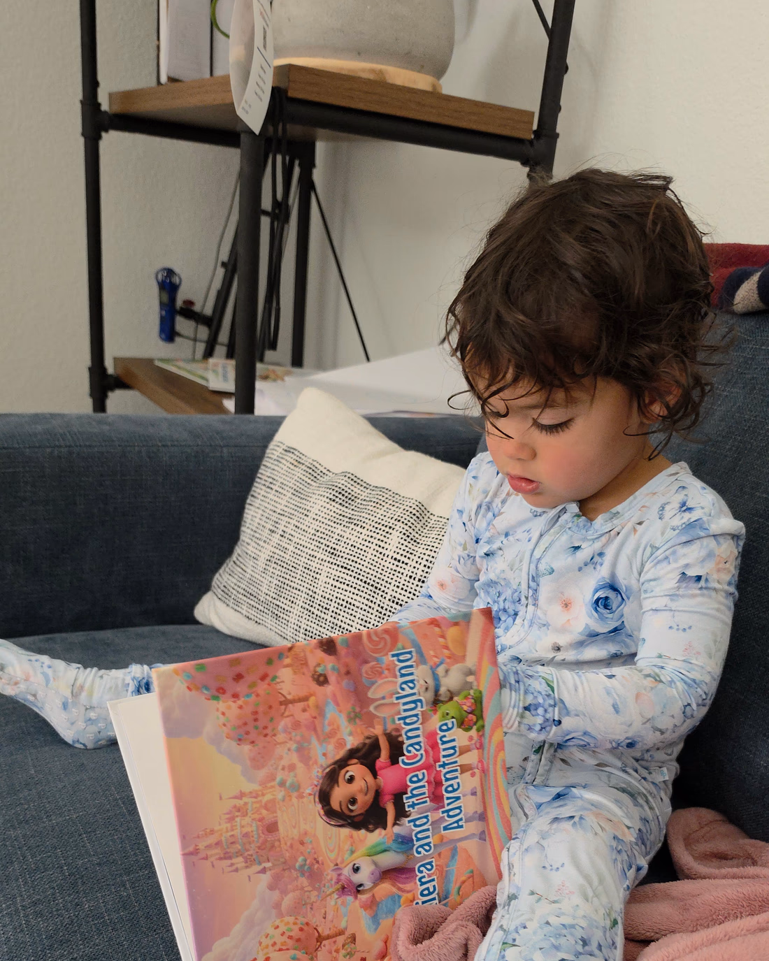 A young girl in pajamas curled up on the couch, reading her personalized Story Genie hardcover